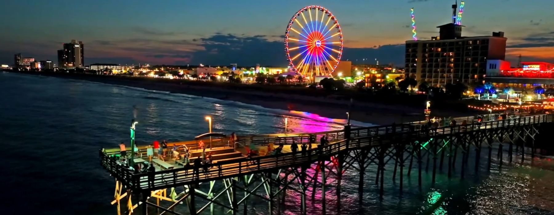 a ferris wheel and a city by a dock by the ocean